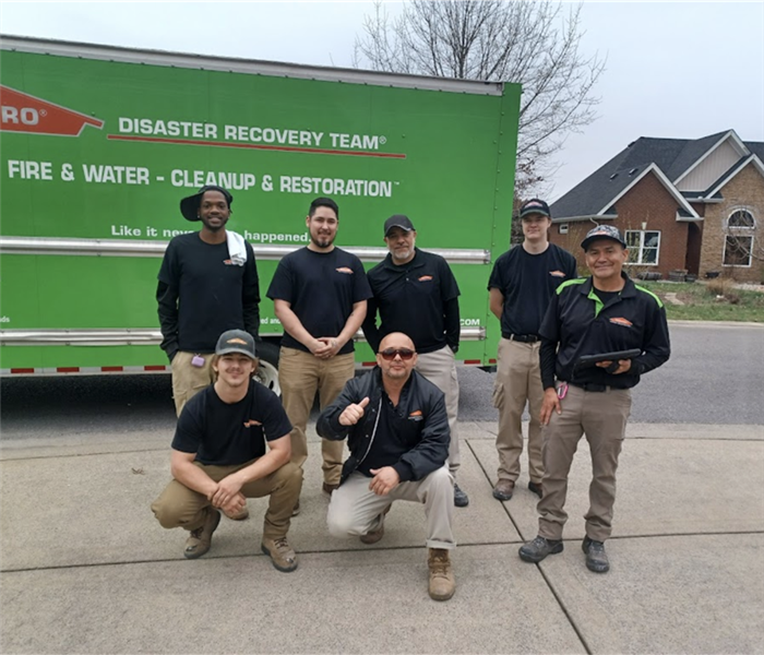 SERVPRO green Disaster Recovery truck parked outside of a water damage restoration project with restoration techs nearby